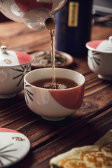 Pouring japanese tea into asian porcelain cup on wood table