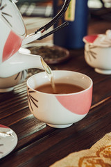 Pouring japanese tea into asian porcelain cup on wood table