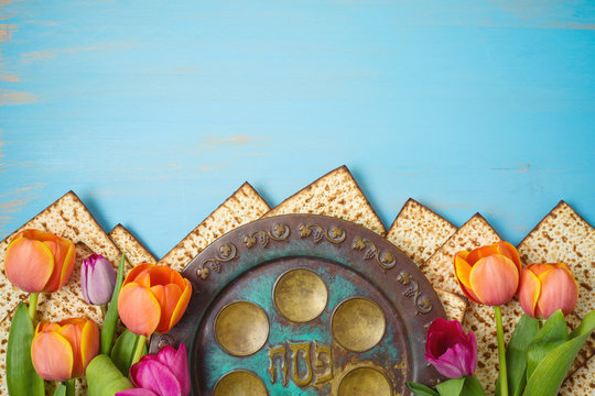 Jewish holiday Passover celebration concept with seder plate, matzah and tulip flowers on wooden table. Pesach background.