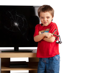 Naughty small boy holding a slingshot standing in front of a TV with broken screen