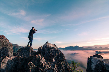 Young asian photography stand on the top of mountain and take the landscape photo during sunrise...