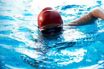 Joyful smiling boy swimmer in a cap and Goggles learns professional swimming in the swimming pool in gym close up