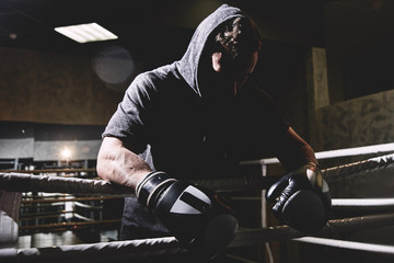 Closeup portrait of a professional boxer in a hood and gloves in the ring. Dark colors, face in shadow