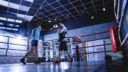 Professional boxers with gloves train fights in indoor boxing ring, dark colors