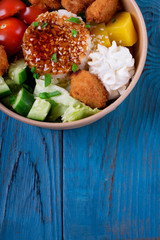 Poke bowl with fried chicken, vegetables and rice on the blue wooden table. Hawaiian cuisine meal