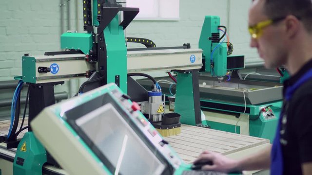 A male operator controls the CNC machine while standing at the control panel. Selective focus.