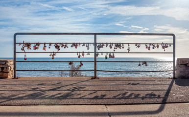 Lovers' locks against the light on a metal railing facing the Mediterranean Sea. Promenade of Cala Millor, island of Mallorca, Spain