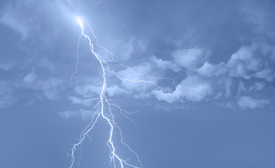 Lightning strikes between blue stormy clouds.