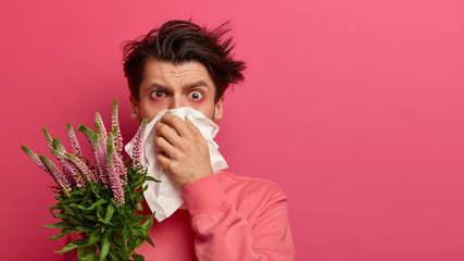 Seasonal allergy and health problems concept. Unhealthy man blows nose in tissue, being sensitive...