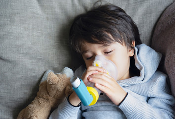 Poor boy tired from chest coughing holding inhaler mask, Child falling a sleep while using the...