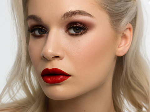 Close-up portrait of the cleanliness face of a beautiful woman with dark burgundy smoky eyes makeup, red full lips. Sexy model with clean shiny skin, clean face, long curly hair. glamorous image