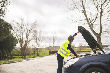 Young Caucasian woman looking at car engine, car broken down in the middle of the road. Automobile...