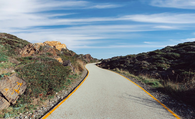 A clear asphalt road with yellow lines that crosses the quiet mountain with clouds in the blue sky