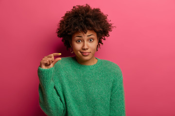 Curly woman measures something tiny, says she has little problems, shapes small obejct, wears green...