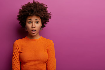 Indoor shot of shocked curly haired woman horrified to find out about awful accident, dressed in...