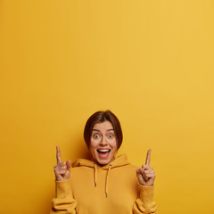 Cheerful pleased Caucasian woman points above, has glad expression, shows nice offer, gives...
