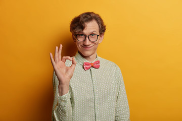 Funny smiling male geek shows ring gesture with fingers, says good job, satisfied with suggestion,...
