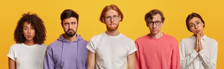 Set of serious displeased diverse people look directly at camera, press lips, one woman beggs for apologise, some of them wear spectacles, stand next to each other against yellow background.