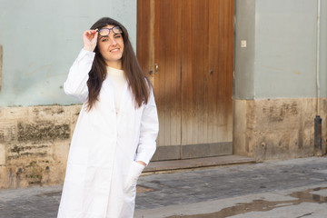 young woman model looks at camera and raising stylish eyeglasses. Pharmacist, therapist, doctor, nurse, veterinarian, ophthalmologist, beautician, healthcare, optometrist, in the city, in white coat u