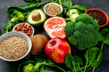 Selection of healthy food: fruits, seeds, cereals, superfoods, vegetables, leafy vegetables on a stone background. Healthy food for humans.
