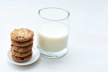 Oatmeal cookies and chocolate chips accompanied by glass of milk