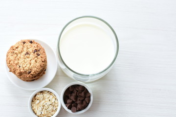 Oatmeal cookies and chocolate chips accompanied by glass of milk