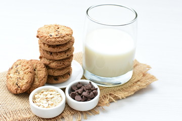 Oatmeal cookies and chocolate chips accompanied by glass of milk