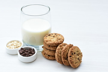 Oatmeal cookies and chocolate chips accompanied by glass of milk