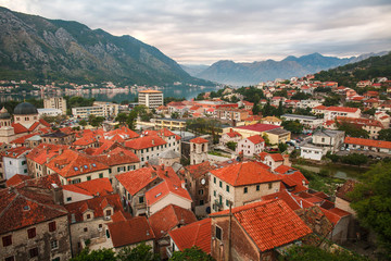 Naklejka na ściany i meble Tops of roofs of the old city of Kotor on background of bay, mountains and sky