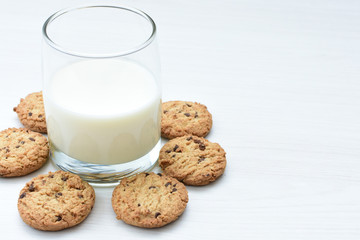 Oatmeal cookies and chocolate chips accompanied by glass of milk