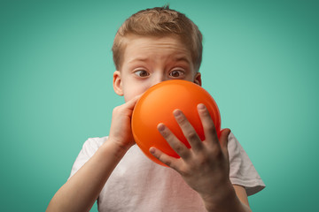 boy in a white t-shirt inflates an orange balloon on a blue background. a child plays with a balloon
