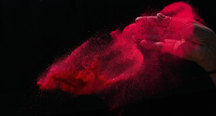 Closeup hand red colour holi powder splash at black background, red paint on Holi celebration