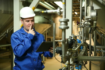 food factory worker is holding a tablet and thinking at plant near the equipment