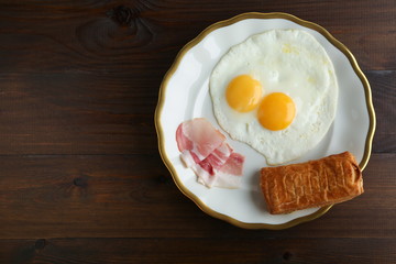 fried eggs, bacon and bread are on the plate on dark wooden background top view with emty space