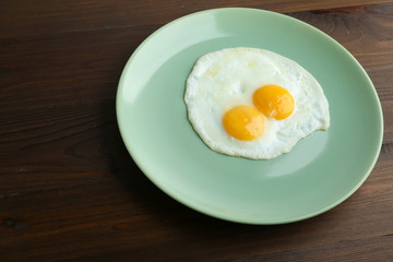 two fried eggs on a green plate on dark wooden background flat lay.