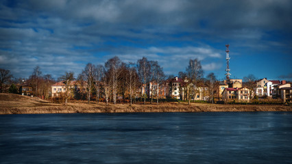 Fototapeta premium Eco-friendly cottage village on the shore of the lake. Bright spring landscape with houses near a frozen lake