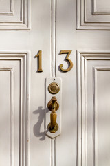 House number 13 on a white wooden front door with bronze door handle