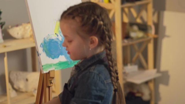 Kids finger painting. Art hobby. Talented girl creating angel work on easel with hands.