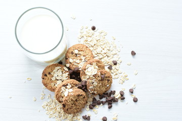 Oatmeal cookies and chocolate chips accompanied by glass of milk