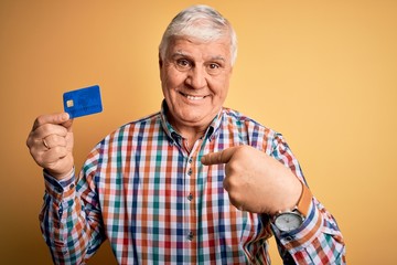 Senior handsome hoary customer man holding credit card to finance payment with surprise face pointing finger to himself