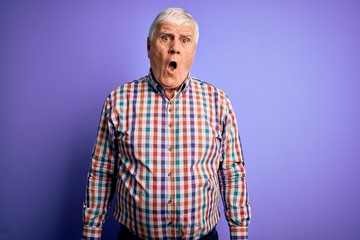 Senior handsome hoary man wearing casual colorful shirt over isolated purple background In shock face, looking skeptical and sarcastic, surprised with open mouth