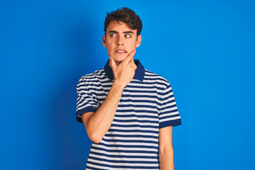 Teenager boy wearing casual t-shirt standing over blue isolated background Thinking worried about a...