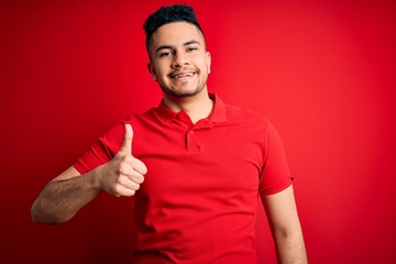 Young handsome man wearing red casual polo standing over isolated background doing happy thumbs up...