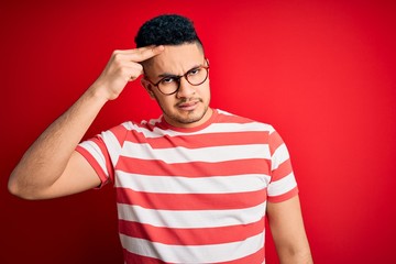 Young handsome man wearing casual striped t-shirt and glasses over isolated red background pointing...