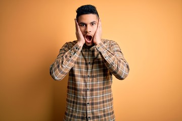 Young handsome man wearing casual shirt standing over isolated yellow background afraid and shocked, surprise and amazed expression with hands on face