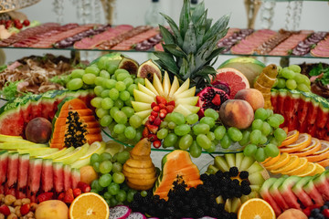 Horizontal images of different fruits on festive tables with grapes, berries, mango, watermelon, pomegranate. Celebration or other event. Wedding table decoration