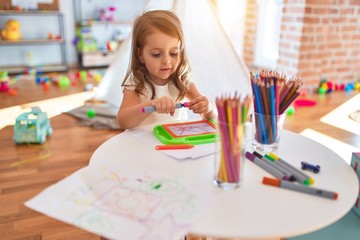 Adorable blonde toddler drawing using digital board around lots of toys at kindergarten