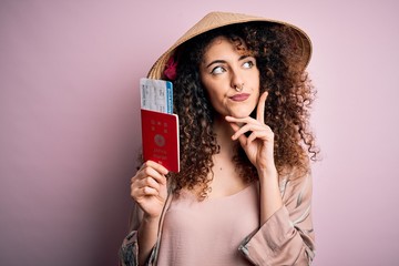 Beautiful tourist woman with curly hair and piercing wearing asian hat holding japan passport...