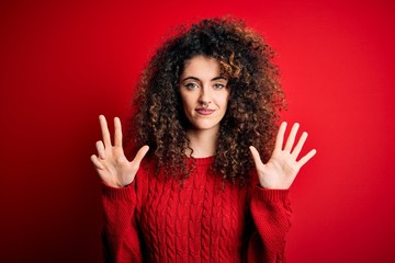 Young beautiful woman with curly hair and piercing wearing casual red sweater showing and pointing up with fingers number eight while smiling confident and happy.