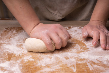 A woman kneads the dough. Plywood cutting board, wooden flour sieve and wooden rolling pin - tools for making dough.